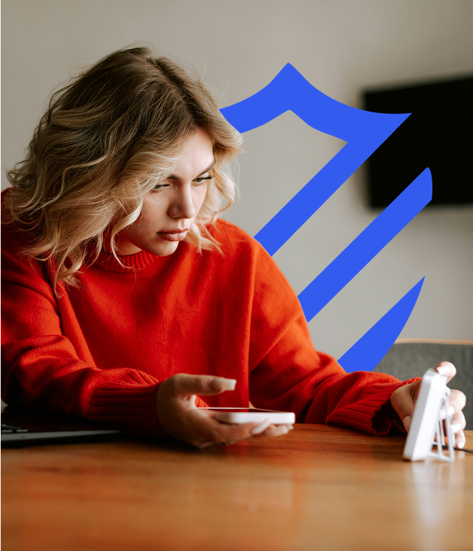 Woman looking at security camera monitor with One Call Alarm logo shield behind her
