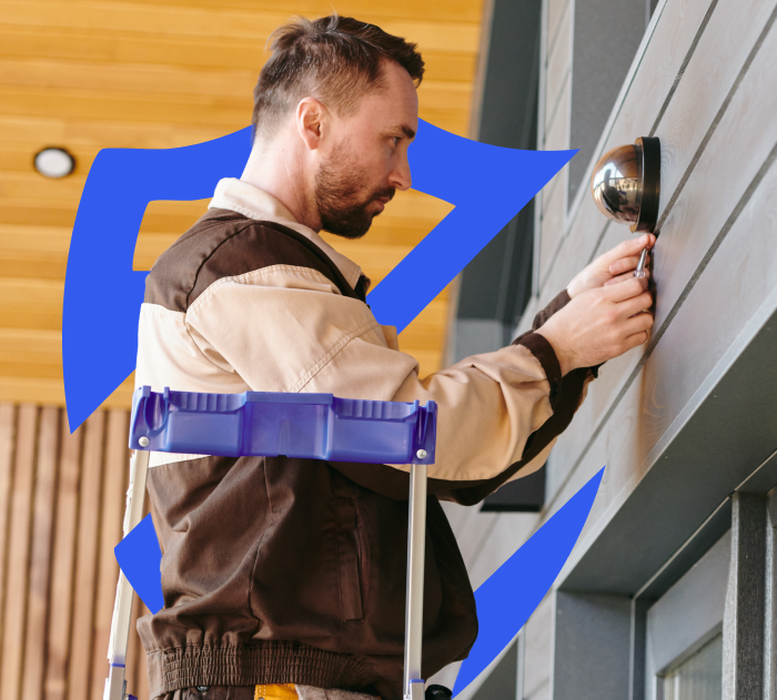 Person hanging surveillance camera with One Call Alarm shield logo behind them